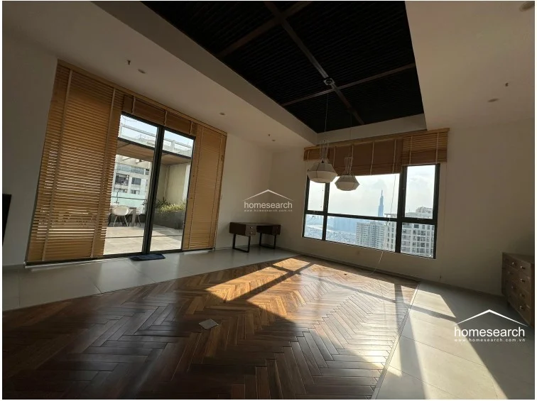 This view of the living room emphasizes the high-contrast design, featuring a dark wood-paneled ceiling inset and matching bamboo blinds on the floor-to-ceiling windows. The room flows directly onto an outdoor balcony, and the overall condition appears well-maintained with modern recessed lighting and dual AC units.