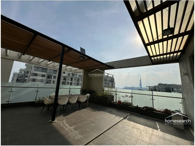 This expansive outdoor terrace offers a perfect space for al fresco dining under a modern slatted pergola. It features dark tiled flooring, built-in planters, and a glass railing that provides an unobstructed, impressive view of the city skyline.