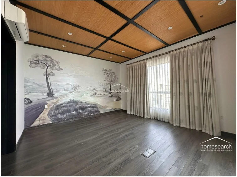 This bedroom showcases an artistic, hand-painted landscape mural on the main wall, complemented by a grid-patterned wood ceiling and dark wood flooring. The room is equipped with an AC unit and floor-to-ceiling curtains, creating a serene and well-maintained atmosphere.