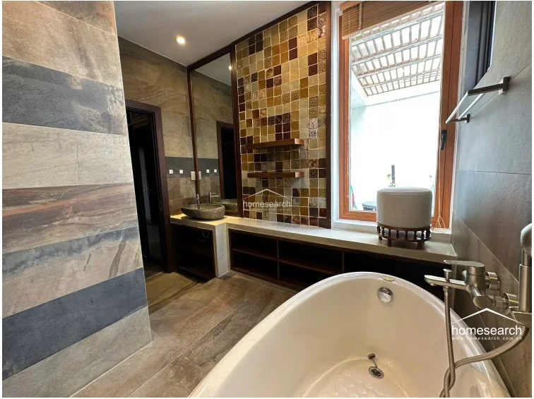 This luxurious bathroom is finished with large-format, multi-toned stone tiles and a decorative mosaic tiled wall behind the vanity. It is equipped with a contemporary freestanding bathtub, a unique stone vessel sink, and open wooden shelving, all maintained to a high standard.