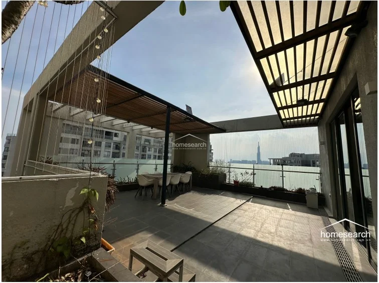 This expansive outdoor terrace features a modern pergola structure, providing a shaded dining area that overlooks the city skyline. The space is finished with durable grey floor tiles and includes integrated planters, making it an ideal setting for outdoor entertaining.
