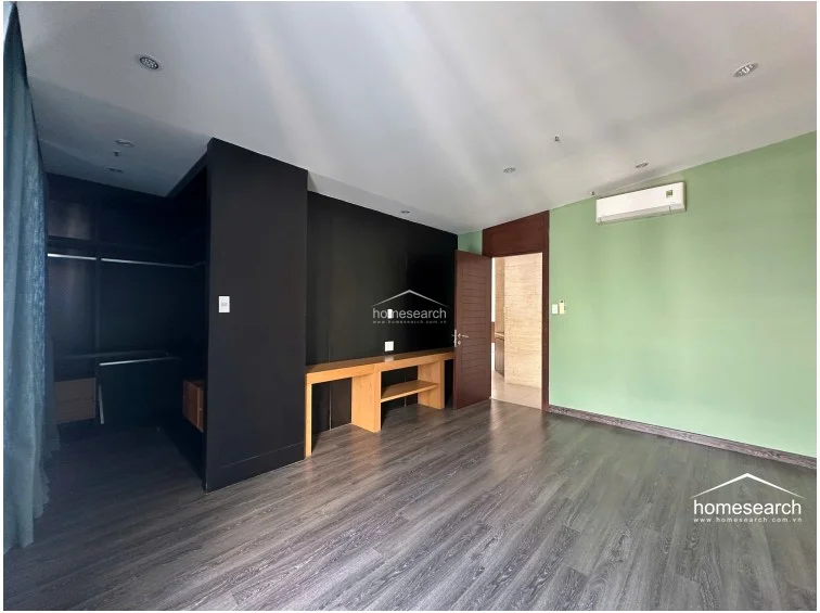 This bedroom provides a clear view of the open-concept walk-in closet area, which features sleek black cabinetry. The room is equipped with a wall-mounted AC unit and a built-in wooden desk, while the sage green and black wall palette creates a modern, high-contrast interior.