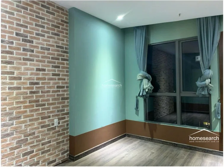 This bedroom features a striking contrast between a textured brick accent wall and soft, sage-green painted walls. The room is fitted with wood-look flooring and floor-to-ceiling windows draped in elegant curtains, offering a cozy yet modern atmosphere.