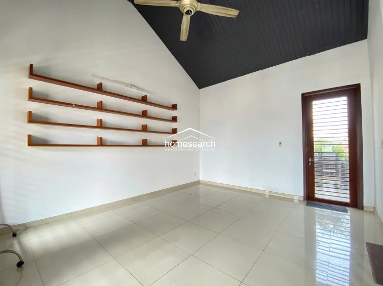 This room features a high, vaulted ceiling with a dark finish and a ceiling fan, creating an airy and architectural focal point. The wall is equipped with extensive built-in wooden shelving, while a glass-paneled door provides direct access to the outdoor area.