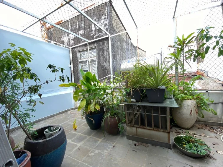This rooftop terrace is a lush, semi-enclosed garden space featuring a variety of potted plants and a small water feature. The area is protected by a wire mesh enclosure, offering a secure and tranquil outdoor retreat with tile flooring.