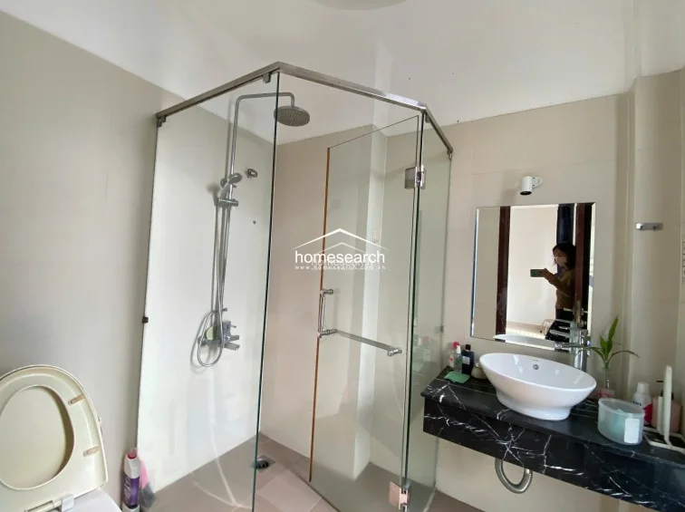 This bathroom features a contemporary glass-enclosed walk-in shower with a rainfall showerhead and a sleek vessel sink set atop a black marble vanity. The room is finished with neutral-toned wall tiles and provides a clean, functional layout with a modern aesthetic.