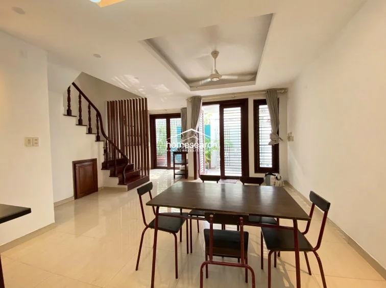 This angle provides a wider perspective of the dining room, showcasing the flow between the living area and the outdoor terrace visible through the glass doors. The room is sparsely furnished, emphasizing the neutral wall finishes and the high-quality wood used in the door frames and staircase structure.