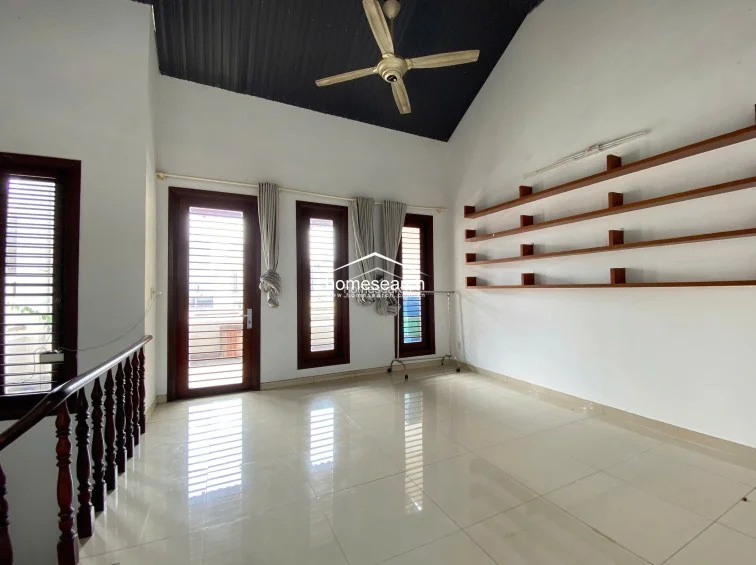 This upper-level landing or lounge area mirrors the vaulted ceiling design, providing a bright and open transition space. It is equipped with multiple windows and a glass door, offering plenty of natural light and access to an outdoor terrace, complemented by simple, functional shelving.