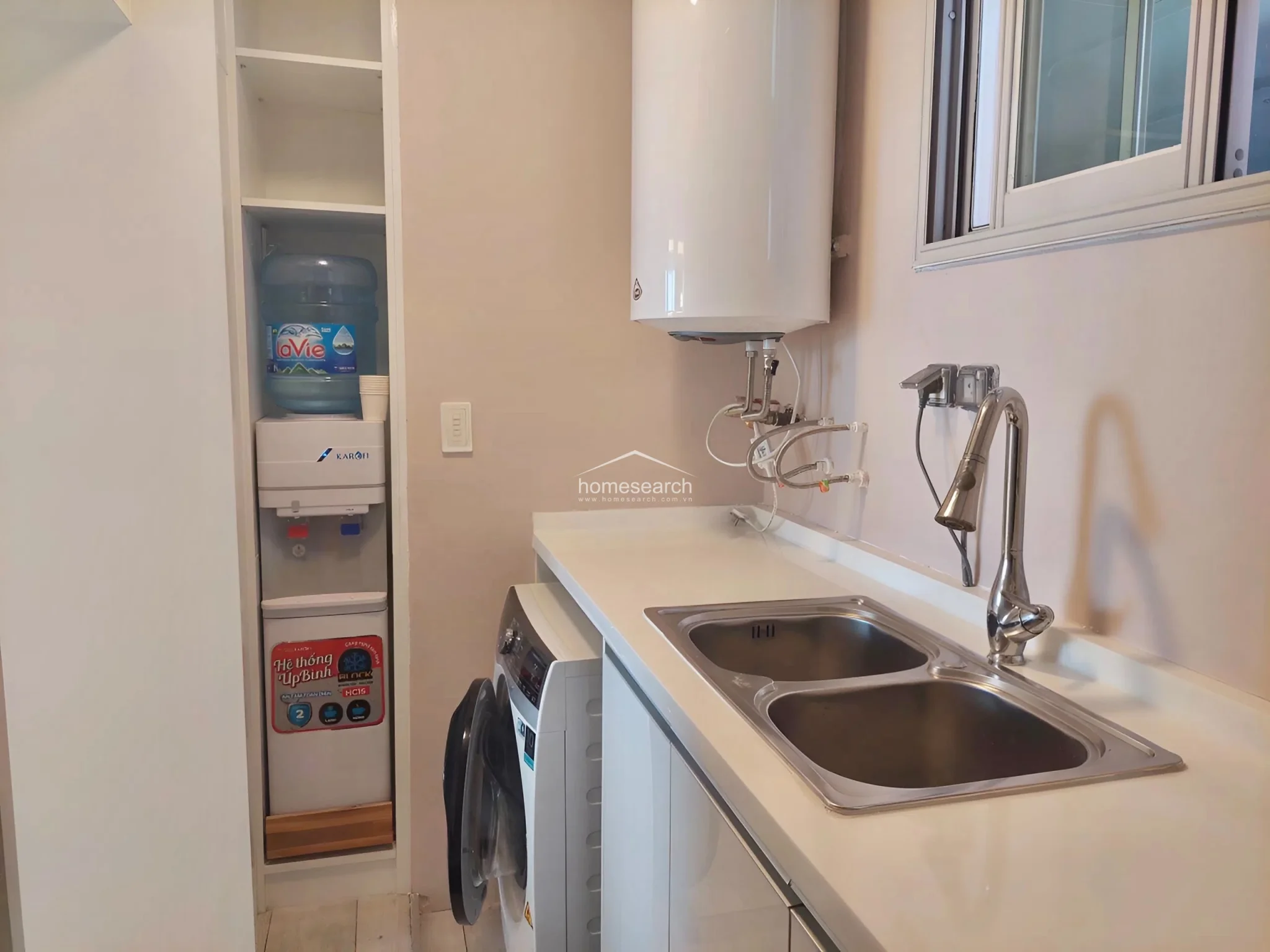 This close-up of the utility area showcases the organized layout, including a dedicated built-in alcove for a water dispenser. The area is well-maintained with white countertops and cabinetry, providing convenient access to plumbing fixtures and essential household appliances.