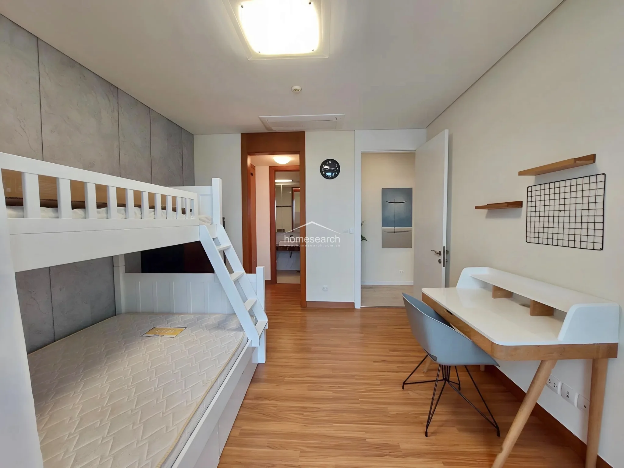 This bedroom features a functional layout with a white bunk bed and a dedicated study area, making it ideal for children or guests. The room is finished with light wood-tone flooring and neutral walls, and it provides direct access to the adjacent bathroom, ensuring a smooth flow between living and utility spaces.