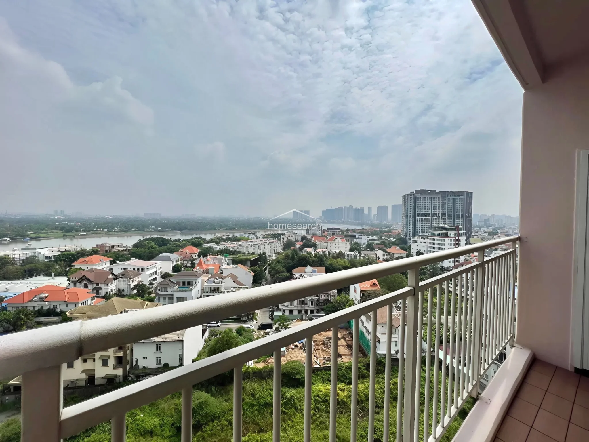 This image captures the same expansive river and city view from a private balcony, emphasizing the property's elevated vantage point. The balcony features a simple metal railing and neutral-toned flooring, providing a clean, open-air space to enjoy the surrounding scenery.