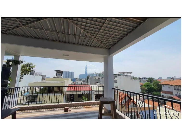 This expansive covered terrace offers an excellent outdoor living space with a metal roof structure and a wrought-iron safety railing. It provides an impressive panoramic view of the city skyline, including a prominent skyscraper, making it an ideal spot for relaxation or entertaining.