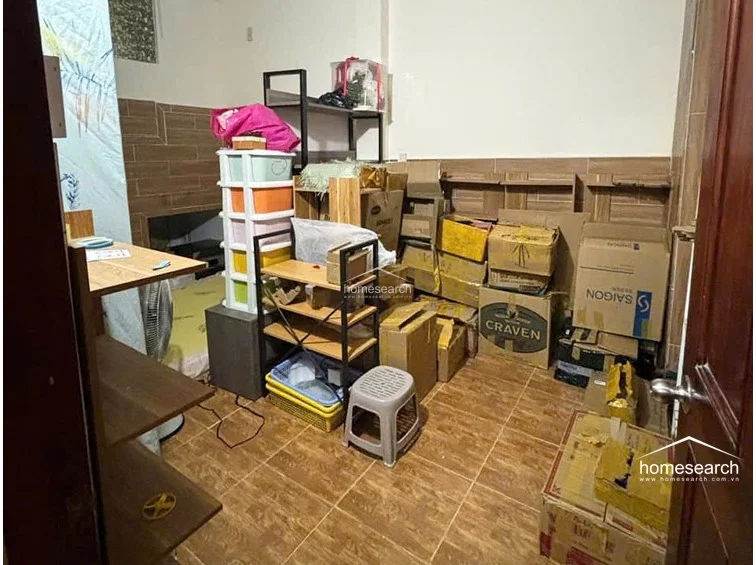 This utility or storage room features brown ceramic tile flooring and matching wall accents, providing a functional, low-maintenance space. It is currently utilized for high-density storage with various cardboard boxes and shelving units, indicating a need for organization to maximize the available floor area.