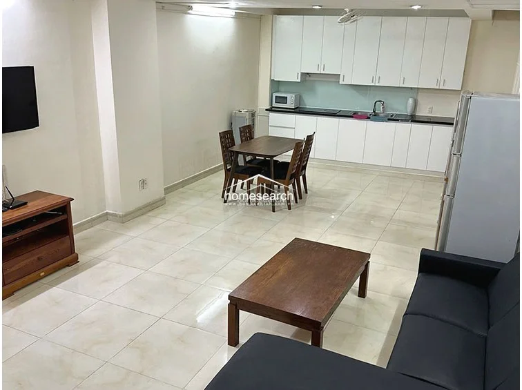 This view captures the functional flow between the kitchen, dining, and living zones, emphasizing the spacious, tiled layout. The area is well-lit by recessed ceiling lights and includes essential appliances like a refrigerator and a washing machine, reflecting a practical and well-maintained living environment.