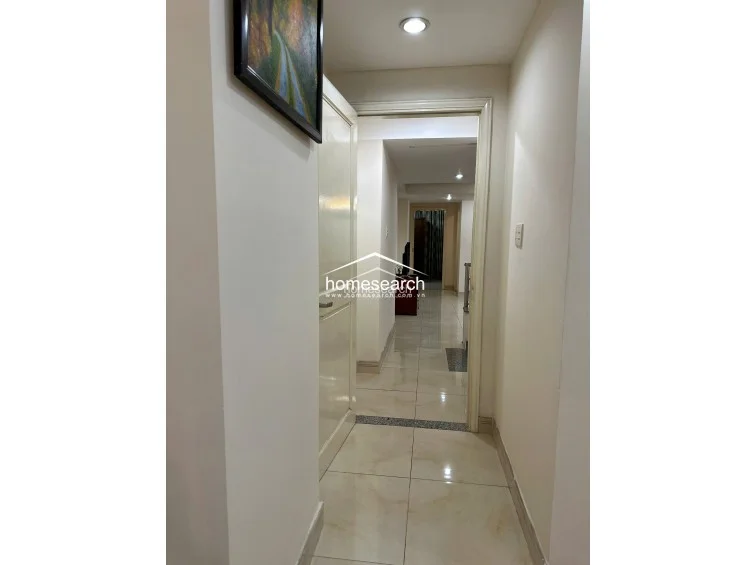 This image captures a transition hallway with light-colored tile flooring and recessed ceiling lighting, connecting various rooms within the property. The neutral wall color and simple architectural lines provide a bright, airy flow that leads the eye toward a glimpse of a living area in the background.