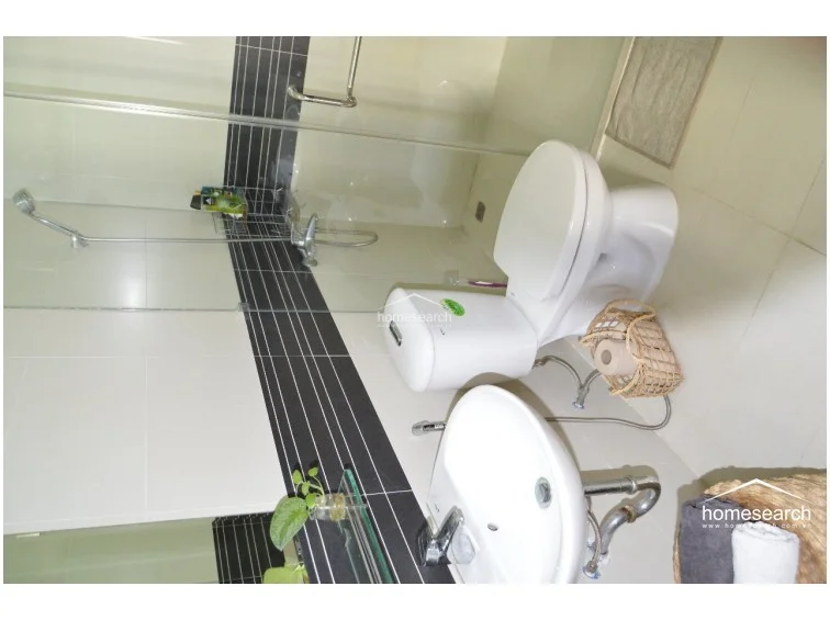 This bathroom features a modern, clean design with a white pedestal sink, a white toilet, and a glass-enclosed shower area. The walls are finished with light-colored tiles accented by a bold, horizontal black tiled stripe, creating a sharp and contemporary aesthetic.