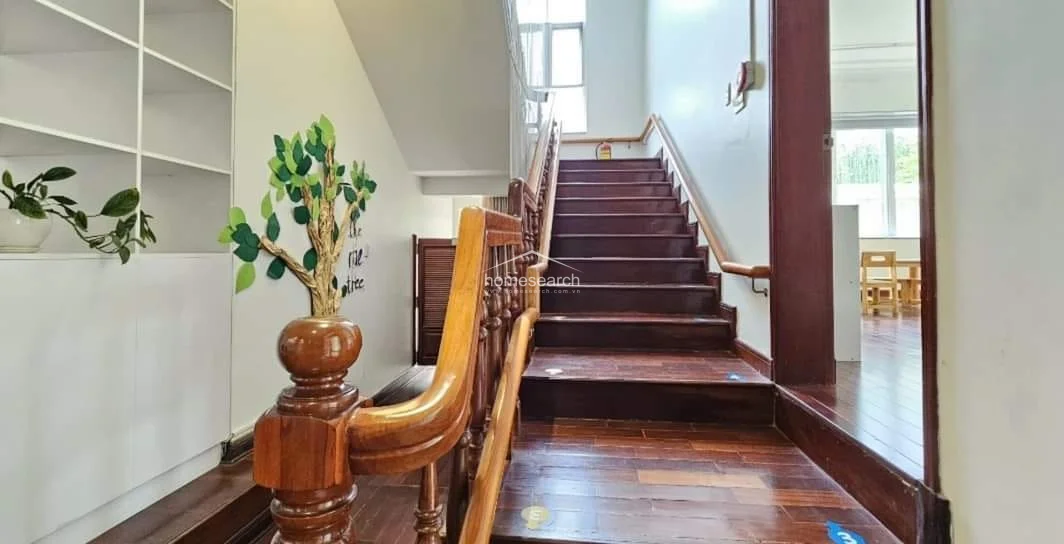 This staircase area features warm wood treads and a matching wooden handrail, connecting the levels with a classic architectural touch. Adjacent to the stairs, a built-in white shelving unit offers organized storage, while the transition to the wooden flooring in the adjoining room maintains a cohesive and well-maintained aesthetic.