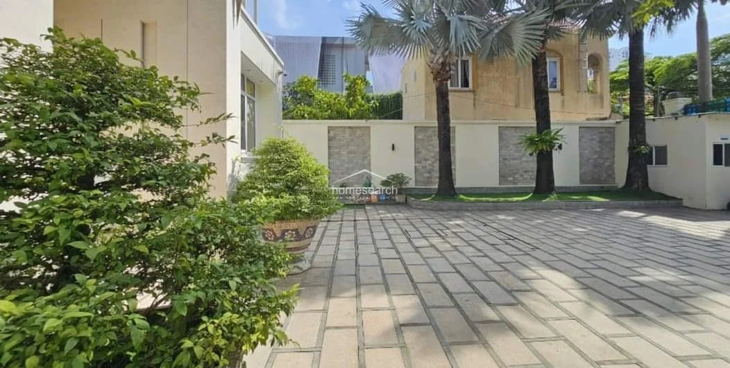This view highlights the expansive, stone-paved courtyard and driveway, which provides ample space for multiple vehicles and outdoor activities. The perimeter walls are accented with textured stone panels and lush landscaping, contributing to a sense of privacy and high-end upkeep for the property.