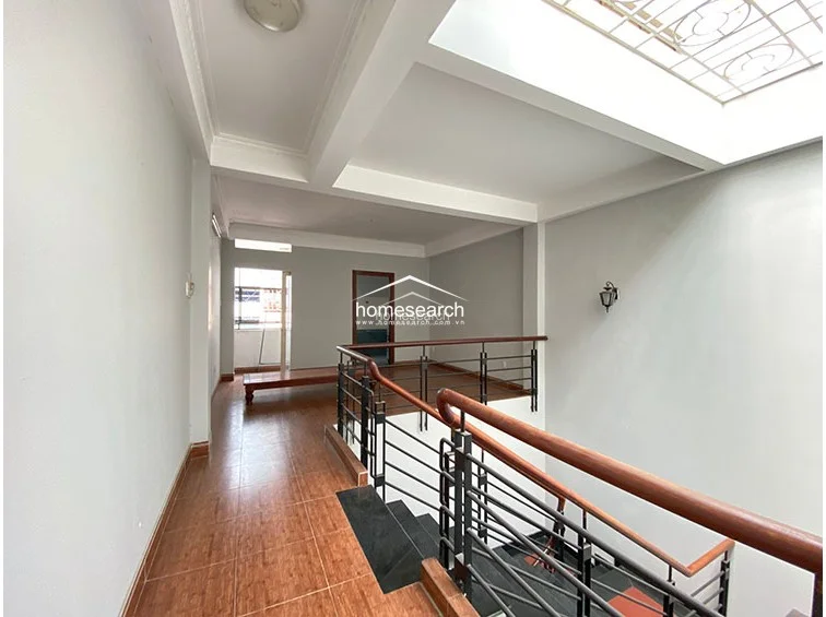 This landing area features an open-plan layout that overlooks the staircase, enclosed by a sturdy metal railing with a wooden handrail. The space is finished with warm-toned tile flooring and includes a skylight above, which allows for significant natural light to filter down into the home.