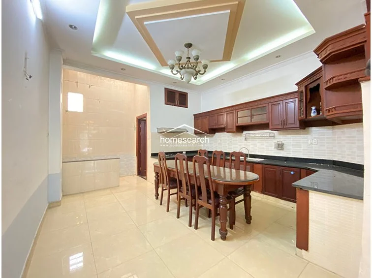 This angle focuses on the kitchen's functional layout, showcasing extensive wood cabinetry that provides ample storage space. The area flows seamlessly into the rest of the home, featuring a clean, polished tile floor and a neutral color palette that highlights the architectural detail of the recessed ceiling.