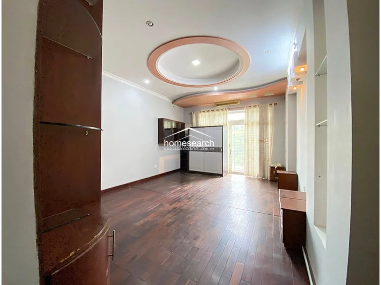 This bedroom space is characterized by light-colored walls and a matching circular ceiling feature, creating a cohesive architectural style. It includes a freestanding wardrobe, a small wooden cabinet, and a glass door leading to an outdoor balcony, which allows for good natural light.