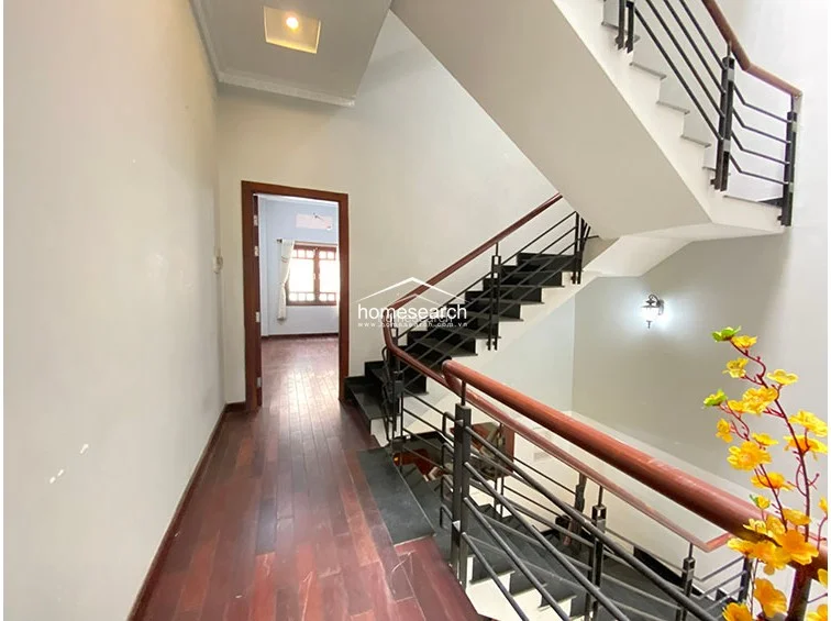 This image captures a central staircase area with dark wooden steps and a metal railing, serving as the main circulation point for the property. The neutral walls and high ceilings contribute to an airy feel, while a decorative floral arrangement adds a touch of color to the landing.