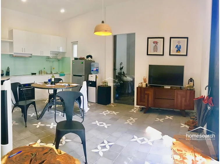 This open-concept living and dining area features stylish patterned floor tiles and a bright, airy atmosphere. The space flows seamlessly into a kitchen area, with a wooden dining set and a cozy sofa arrangement providing a functional layout for daily living.