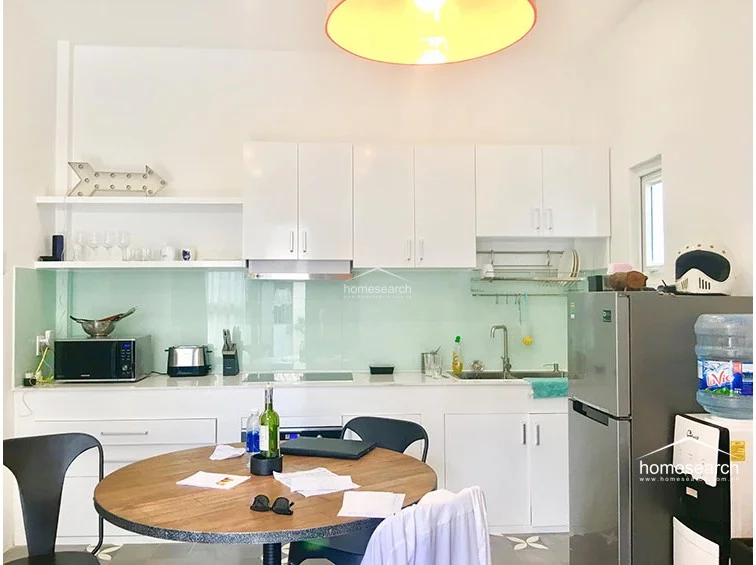 The kitchen is efficiently designed with white cabinetry, a light green glass backsplash, and a clean, minimalist aesthetic. It is equipped with essential appliances, including a microwave and an electric stove, and opens directly into the dining area, making it ideal for compact, modern living.