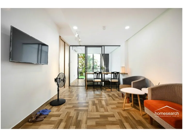 This view highlights the studio's efficient flow, showcasing the transition from the living and dining area to the glass-enclosed bedroom. The wood-patterned flooring provides a warm, cohesive look, while the track lighting and neutral color palette contribute to the unit's well-maintained and modern appearance.