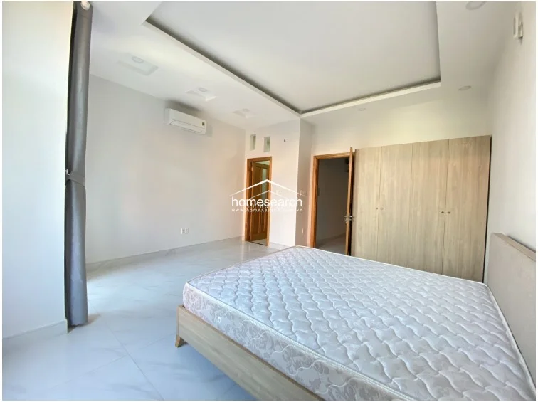 This view of the bedroom highlights the functional layout, showcasing a large, light-wood built-in wardrobe that offers significant storage space. The room is well-maintained with recessed ceiling lighting and a neutral color palette that creates a bright, airy atmosphere.