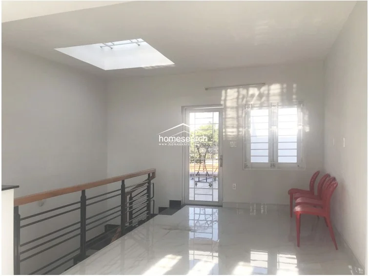 This landing area features bright white walls, polished light-colored tile flooring, and a skylight that provides ample natural illumination. It includes a staircase with a wooden handrail and black metal balusters, connecting to an outdoor balcony through a glass-paneled door.