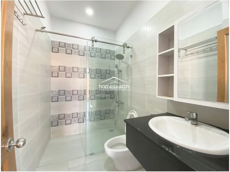 This modern bathroom features a sleek glass-enclosed shower stall with decorative accent tiles and a floating black vanity with a white ceramic sink. The space is well-maintained, utilizing light grey wall tiles and a mirrored medicine cabinet with integrated shelving for storage.