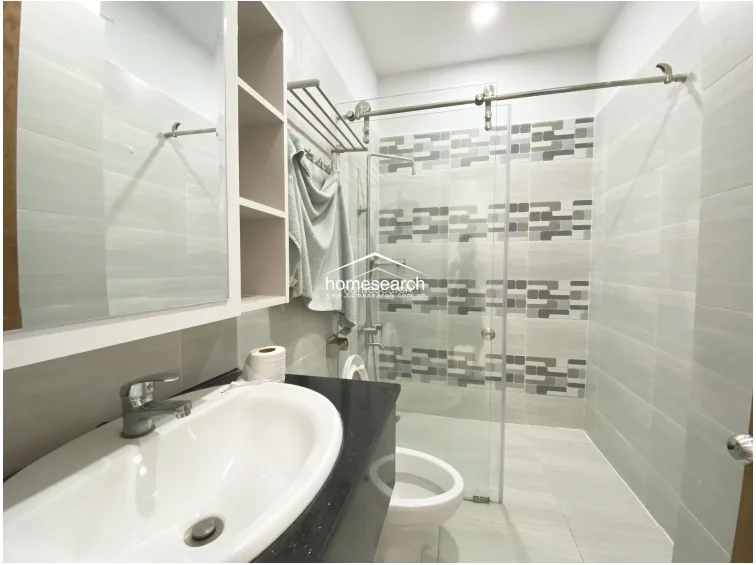 This bathroom maintains a consistent contemporary aesthetic with light grey wall tiles, a glass-enclosed shower, and a black vanity countertop. It includes a wall-mounted towel rack and a mirrored cabinet, ensuring a clean, functional, and organized environment.