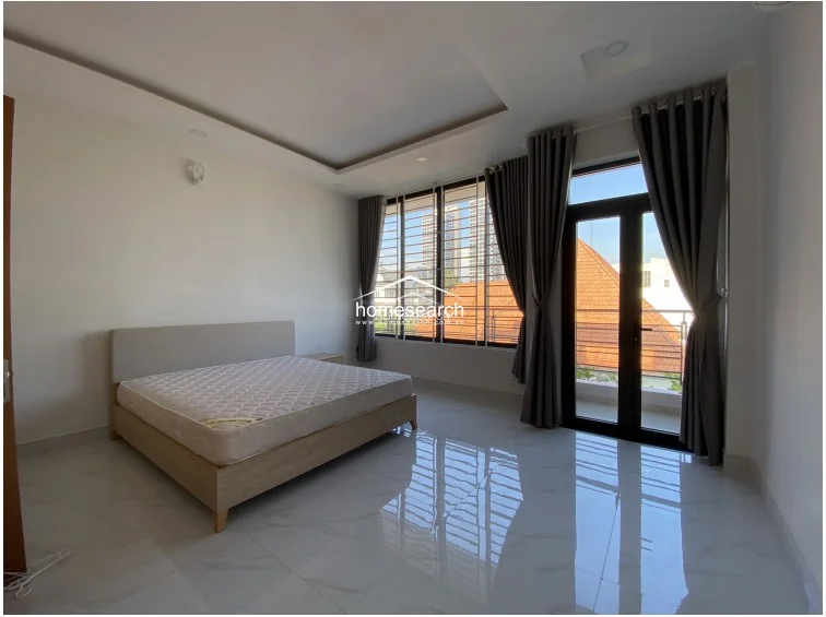 This bedroom mirrors the layout of the previous space, offering a bright and airy atmosphere with expansive windows and a balcony access point. The room is finished with crisp white walls and high-gloss tile flooring, presenting a well-maintained, contemporary living space ready for personalization.