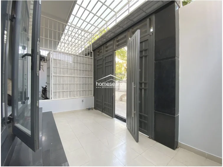 This image shows a secure, covered entryway or porch area featuring durable light-colored tile flooring and high-quality dark metal security doors. The space is protected by a metal-framed roof structure with glass blocks, providing natural light while maintaining privacy and security. The overall condition appears excellent, with a clean, modern aesthetic and well-maintained finishes.