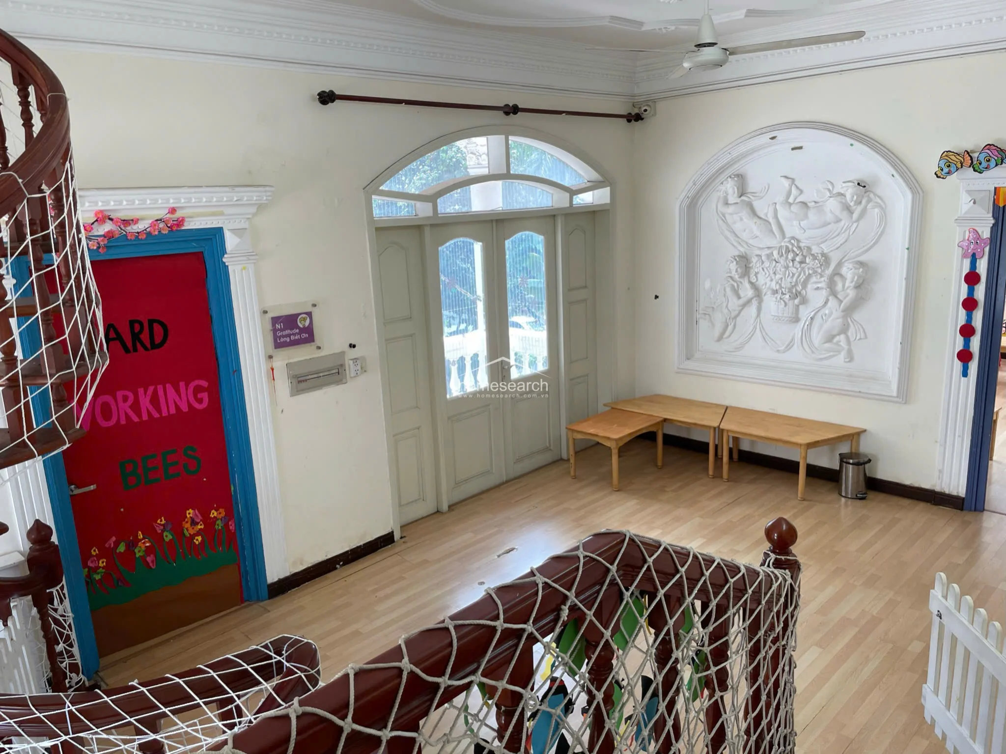 This hallway or foyer area is defined by a large, intricate white wall relief sculpture and light wood laminate flooring. It provides a transition between spaces, featuring an arched doorway and a large windowed entrance that contributes to an airy, well-lit atmosphere.
