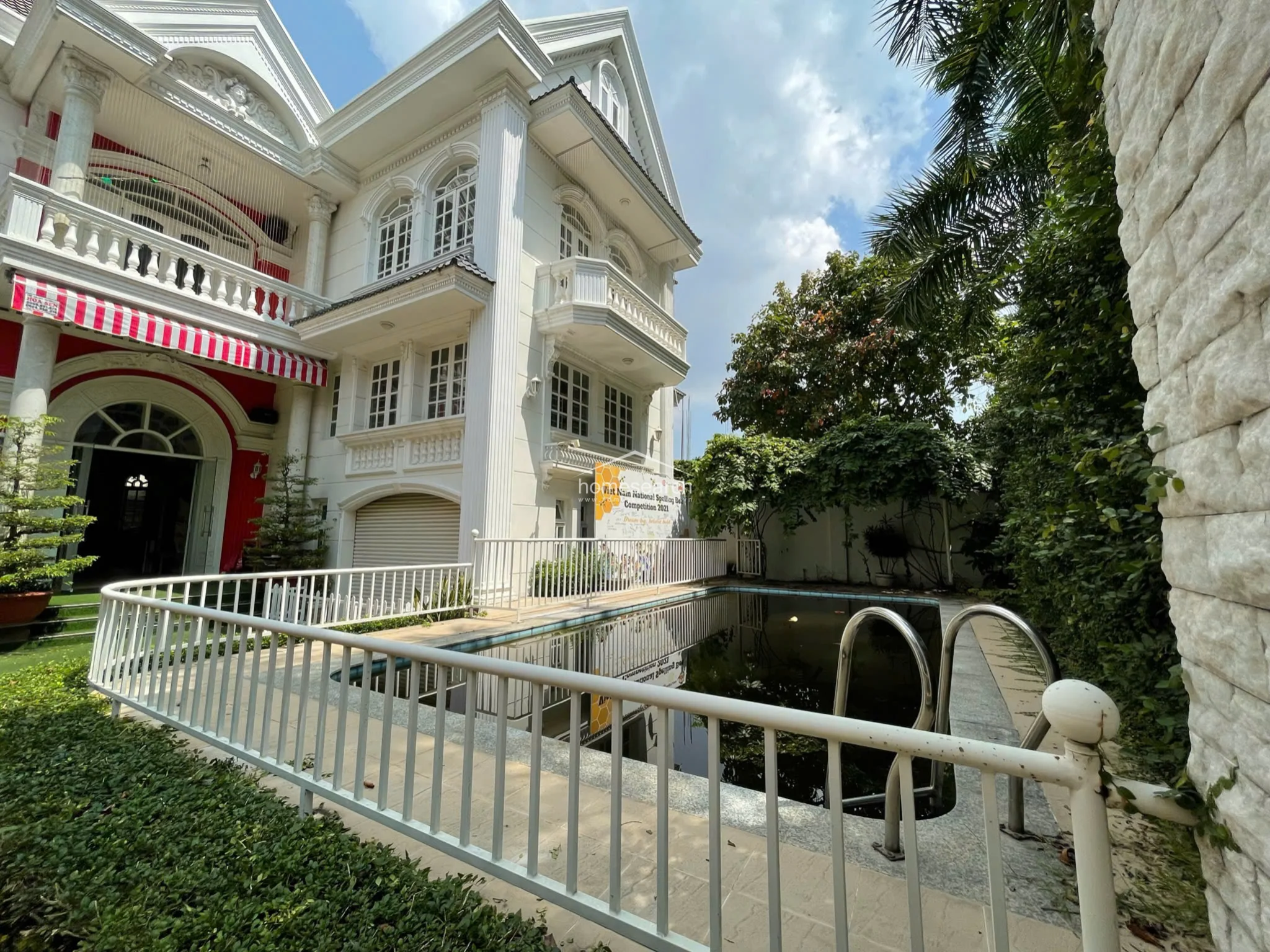 This side view provides a clear look at the villa's verticality, showcasing the multiple levels of balconies and the repetitive, rhythmic placement of windows. The pool area is positioned directly adjacent to the house, though the current state of the water suggests that the outdoor amenities require professional cleaning and restoration to match the prestige of the building's architecture.