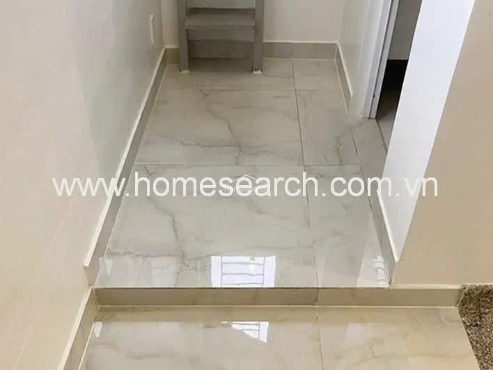 This image captures a transition area or entryway featuring polished, light-colored marble flooring with subtle veining. The space includes a small step-up leading to an adjacent room, creating a distinct separation between zones. The area is clean and well-maintained, reflecting a polished and contemporary architectural style.