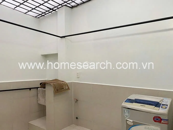 This utility or laundry area features a functional layout with a dedicated space for a washing machine and a built-in basin. The room is finished with neutral-toned wall tiles and white paint, and it includes overhead metal bars for air-drying laundry under a semi-open roof structure.