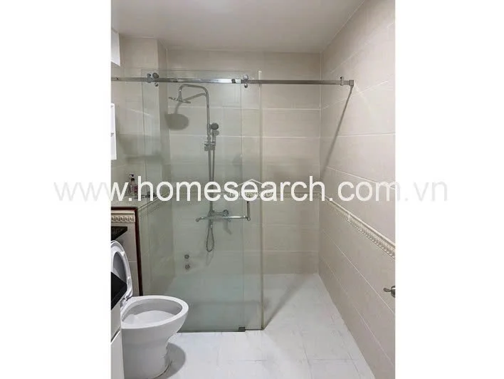 This modern bathroom features a clean, minimalist design with light-colored wall and floor tiles that create a bright atmosphere. It is equipped with a glass-enclosed walk-in shower, a standard white toilet, and a sleek sliding door mechanism for the shower partition.
