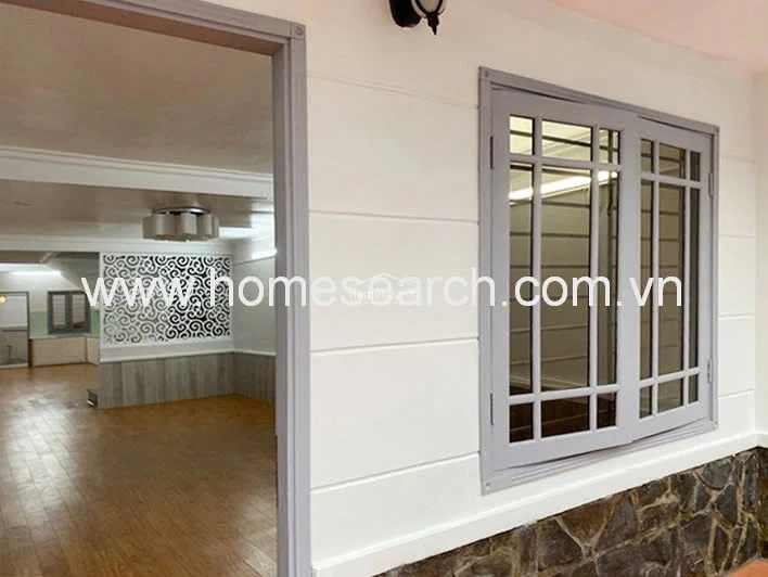 This view captures the interior transition space, highlighting a clean, modern aesthetic with white walls and grey-framed windows. The flooring consists of warm-toned wood-look planks, and the space connects directly to an open-plan living area featuring decorative wall paneling.