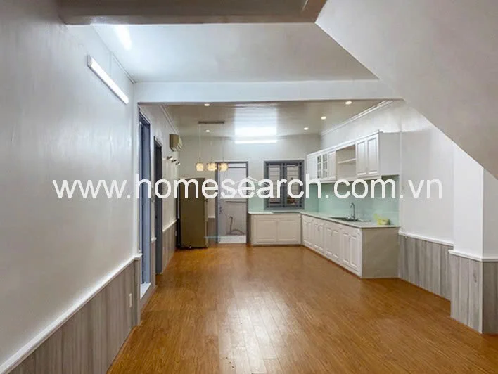 This wide-angle shot reveals an open-concept kitchen and living area that benefits from ample natural light and a clean, minimalist design. The kitchen is equipped with white cabinetry, light countertops, and a glass backsplash, while the overall space is finished with wood-look flooring and neutral wall tones.