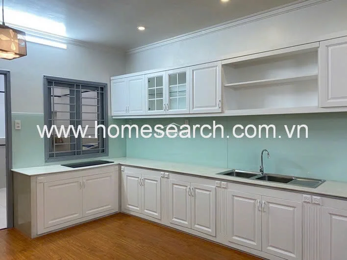 This close-up of the kitchen showcases high-quality cabinetry with a mix of solid and glass-fronted doors, providing both concealed and display storage. The area features a light-colored countertop, a double-basin stainless steel sink, and a sleek, pale green glass backsplash that adds a contemporary touch to the workspace.