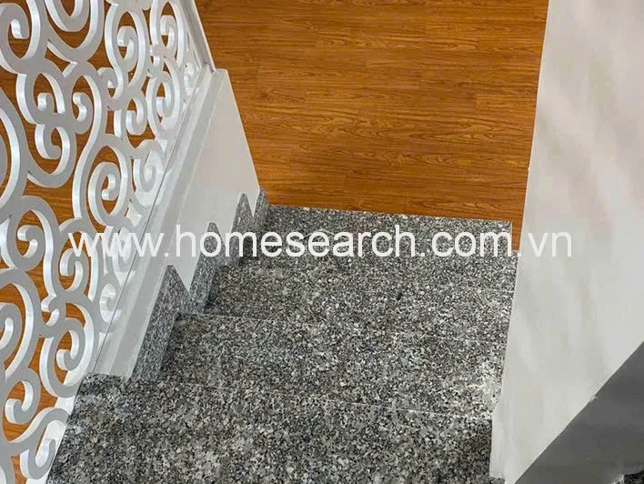 This detail shot focuses on the staircase design, which features sturdy granite steps and an ornate, white laser-cut metal railing. The contrast between the speckled stone stairs and the warm wood flooring on the landing creates a sophisticated transition between levels.