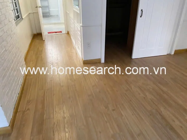 This view highlights the transition between the main living area and an adjoining room, emphasizing the warm wood flooring and clean, minimalist wall finishes. The space is bright and airy, with a clear line of sight through the open doorway. The maintenance level is high, showcasing a tidy and well-kept interior environment.