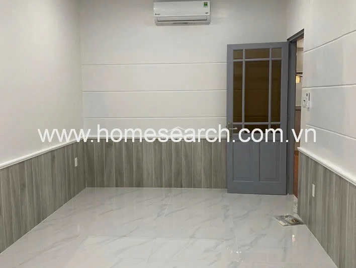 This room features a sophisticated design with white marble-look tile flooring and lower wall paneling in a light wood grain finish. A grey-framed glass door provides a stylish entry point, while a wall-mounted AC unit ensures climate control. The room feels bright and modern, benefiting from neutral tones and high-quality finishes.