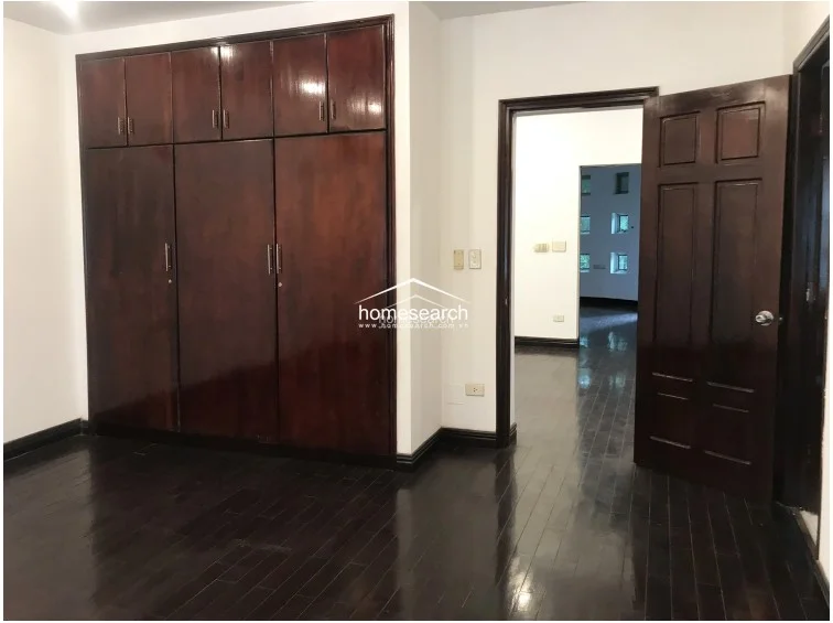 This bedroom features extensive floor-to-ceiling dark wood cabinetry, providing significant integrated storage space. The room maintains a consistent design language with dark hardwood flooring and a matching wooden door, leading seamlessly into the circular room seen in the background.