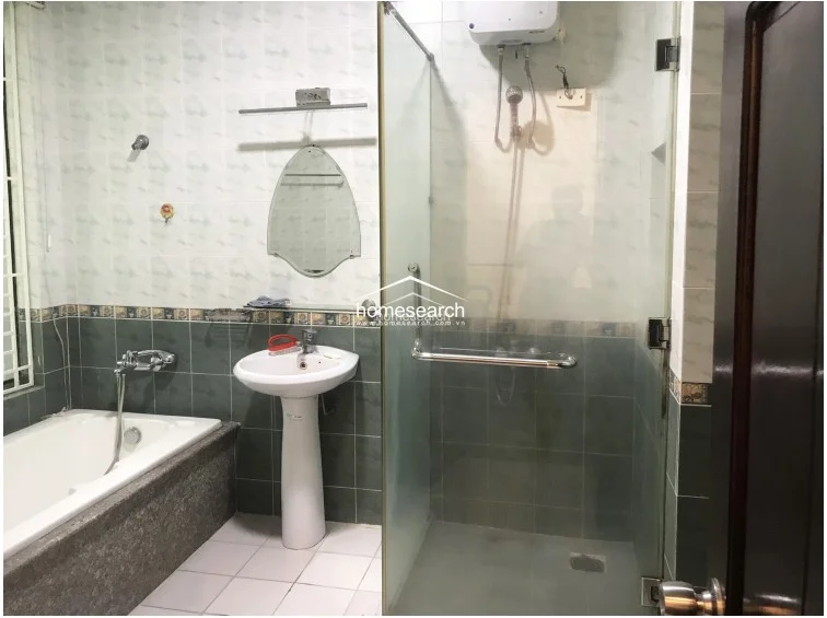 This bathroom features a functional layout with a pedestal sink, a separate bathtub, and a glass-enclosed shower stall. The walls are finished with a two-tone tile design, and the space includes an electric water heater mounted above the shower area for convenience.