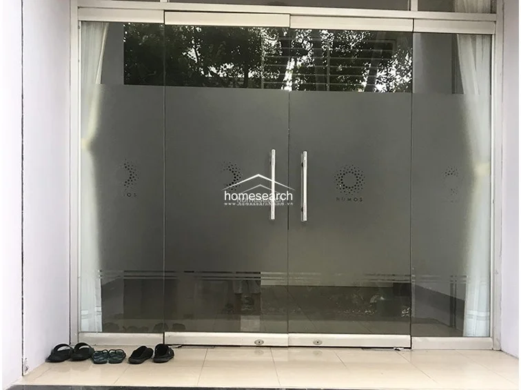 The entrance features double glass doors with frosted privacy film and modern metal handles, presenting a professional and clean aesthetic. The transition from the outdoor area to the interior is smooth, with light-colored tile flooring extending throughout the threshold.