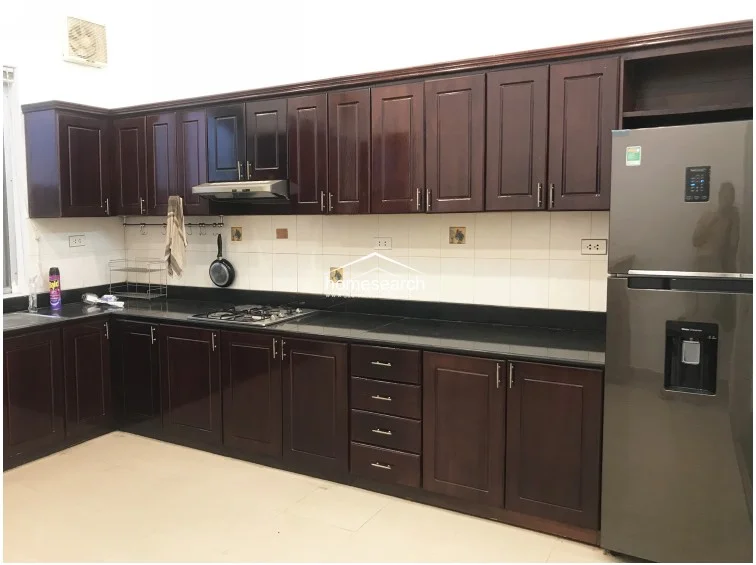 The kitchen is equipped with extensive dark wood cabinetry that provides ample storage, paired with a sleek black granite countertop. It includes a built-in gas stove, a stainless steel range hood, and a modern full-size refrigerator, all set against a neutral tiled backsplash for a functional and tidy cooking environment.